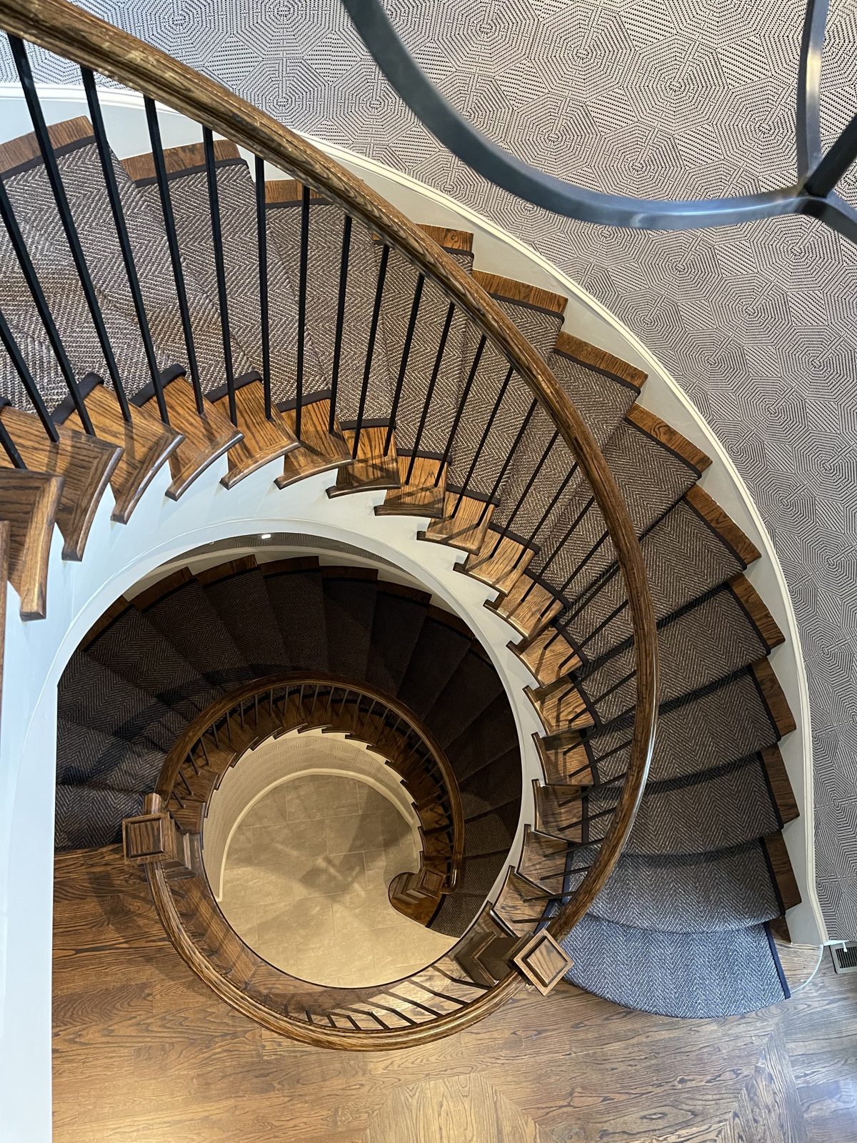 Dramatic spiral staircase with gray patterned runner viewed from above