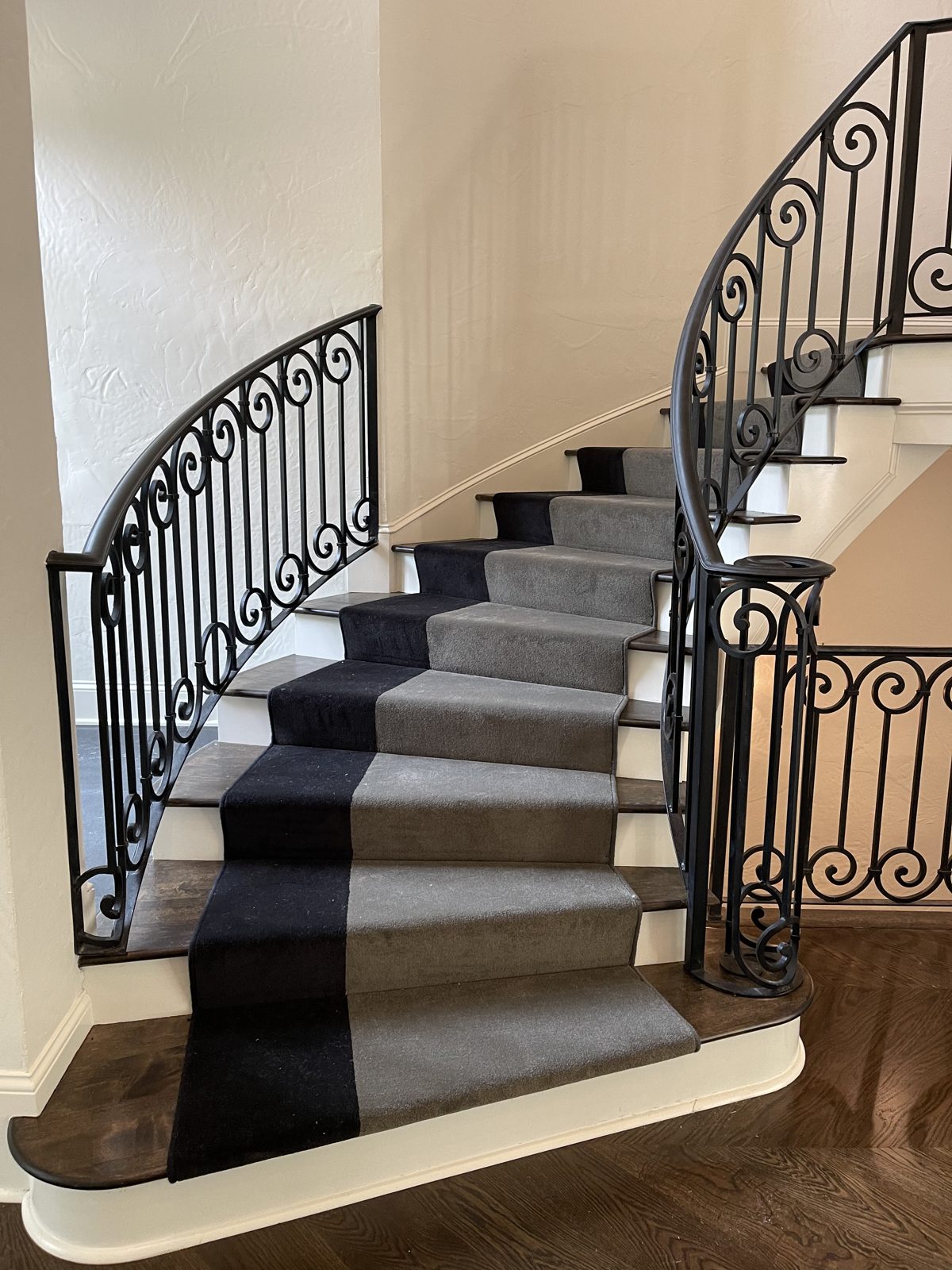 Gray stair runner on a curved staircase with an ornate iron railing